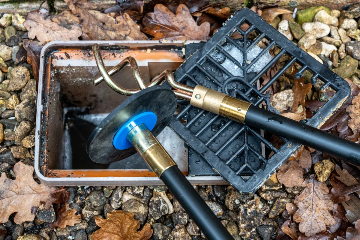 Drain rods with screw and plunger attachments beside an access chamber.