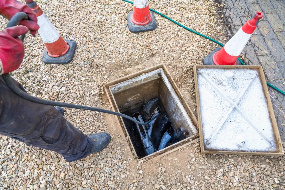 A drainage worker clearing an open inspection chamber on a gravelled area in the UK.