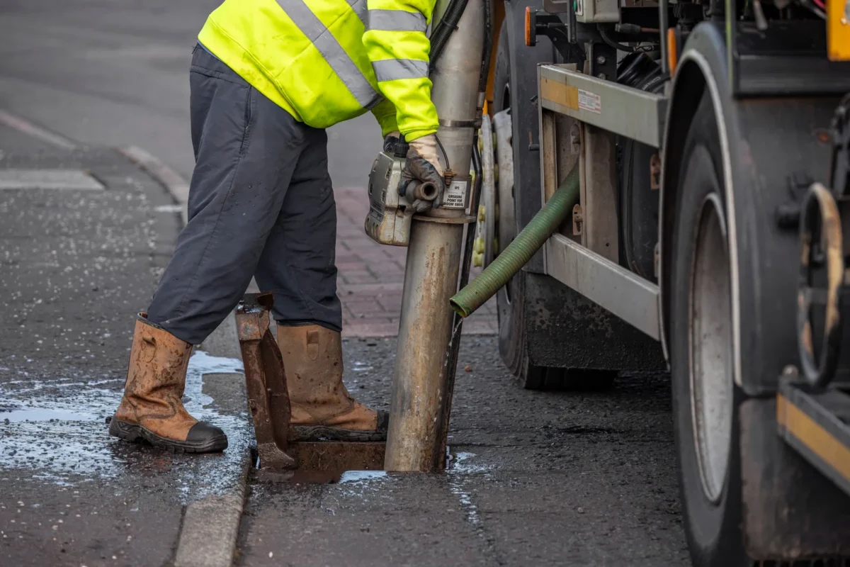 Tanker operative using a suction pipe to clean a roadside gully
