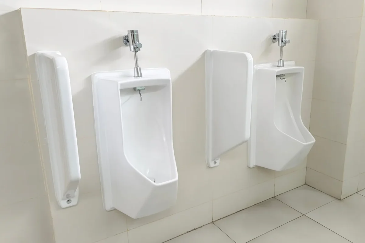 White wall-mounted urinals and flush fittings in a commercial washroom.